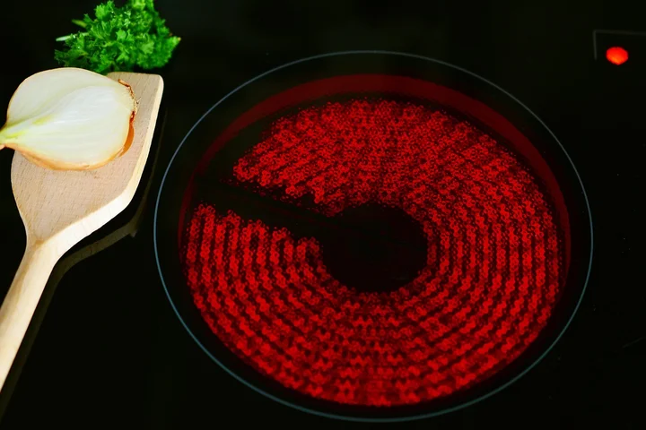 Electric stove burner glowing red with a wooden spoon and half onion on the counter nearby