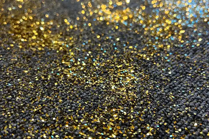 Close-up of dark carpet fibers with gold and multicolor glitter embedded among the threads.