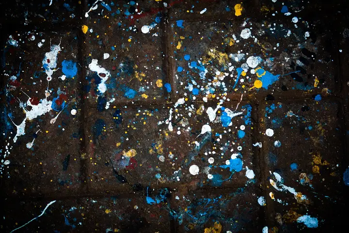 Dark brick wall covered in multicolored paint splatters, representing stains such as protein, oil, and starch.