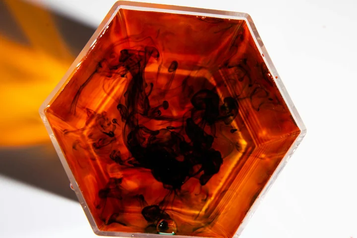 Hexagonal clear container with orange liquid and dark swirls, evoking enzymatic action on stains.