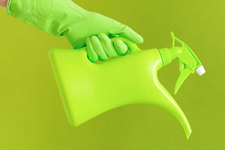 Gloved hand gripping a neon green spray bottle against a lime-green background