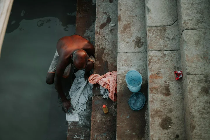 Person washing clothes by hand on stone steps beside a body of water.