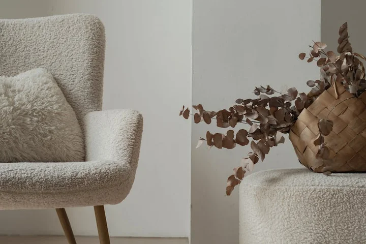 Cream upholstered chair and a woven basket with dried leaves in a minimalist living space.