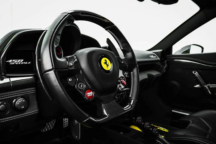 Interior of a high-performance sports car with a carbon fiber dashboard and leather seats, featuring a steering wheel with a yellow Ferrari emblem.