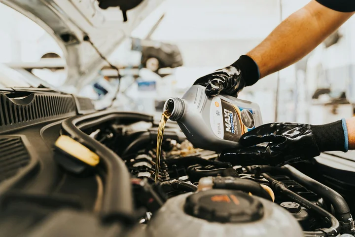 Person wearing gloves pouring motor oil from a bottle into a car engine under the hood