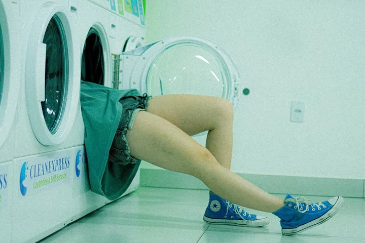 Person in sneakers leaning into a front-loading washing machine in a laundromat