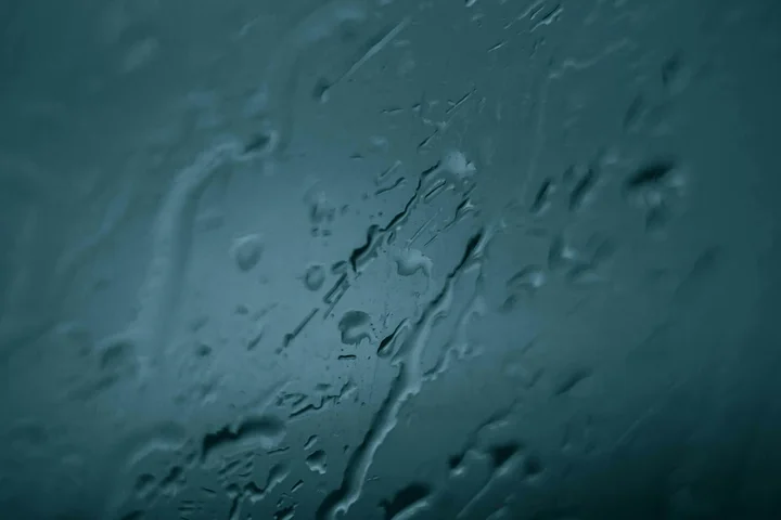 Close-up of glass surface with water droplets and mineral streaks in a blue-green hue.