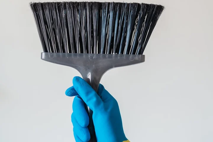 Close-up of a blue-gloved hand gripping a black-bristled cleaning brush.