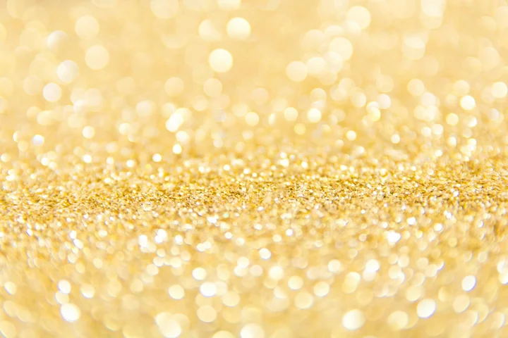 Close-up of gold glitter with soft bokeh lights, creating a sparkling textured surface