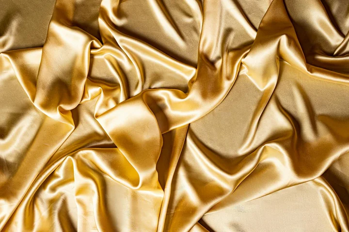 Close-up of shiny gold satin fabric with soft folds
