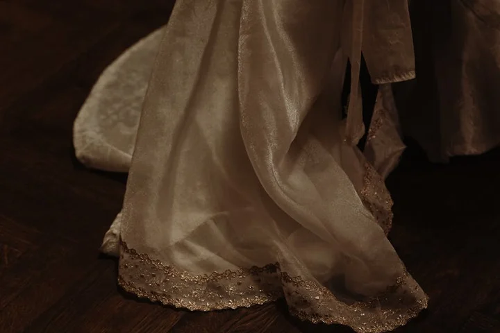 Close-up of cream-colored fabric with lace trim draped on a dark wooden floor