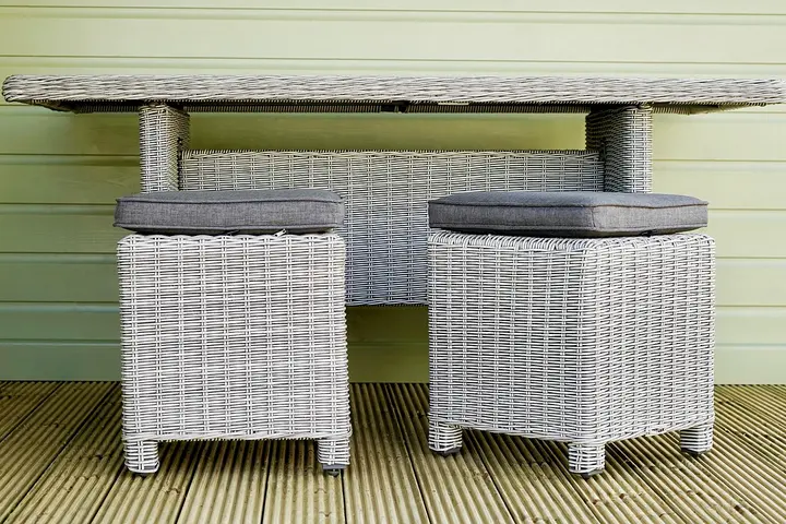Outdoor wicker dining table with matching stools on a wooden deck