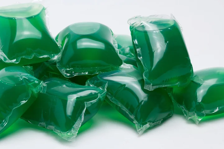 Close-up of glossy green laundry detergent pods wrapped in clear plastic.