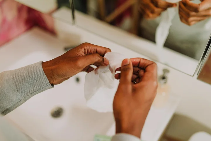 Person blotting a cleaning cloth at a bathroom sink, preparing to remove hair dye stains from the countertop