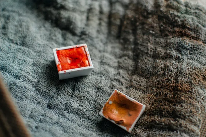 Two small open boxes of red and orange hair dye on a textured blue-gray fabric.