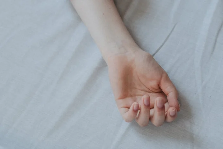 Close-up of a pale hand resting on a white bedsheet, ready to blot a spill.