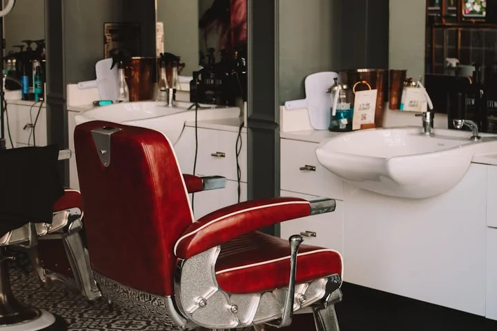 A vintage red barber chair with white sinks in the background, illustrating a classic upholstered piece to test before cleaning.