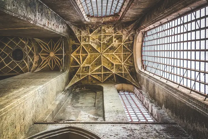Interior view of a dusty, aged cathedral ceiling with ornate stone vaults and metal-grid skylight windows