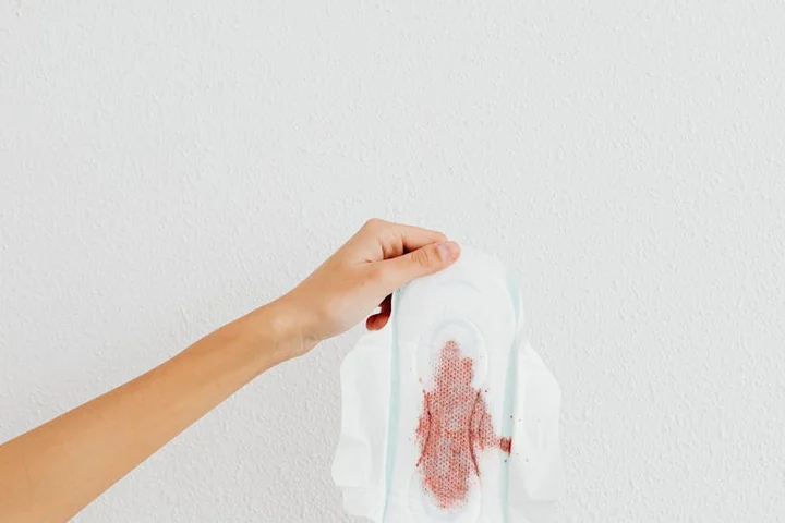 A hand holding a white tissue with a dried blood stain against a pale wall