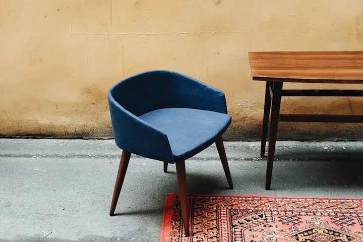 Blue upholstered chair with wooden legs in a room featuring a wooden table and a patterned rug