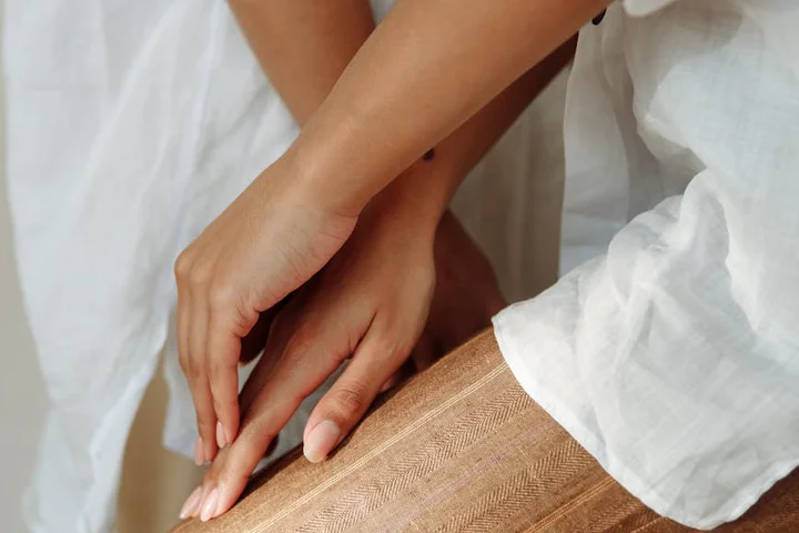 Close-up of hands smoothing sheer beige hosiery on a leg, with a white shirt sleeve nearby.
