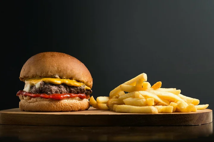 Hamburger with cheese and a side of french fries on a wooden board.