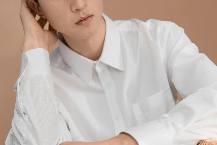 A person wearing a white button-down shirt, seated and looking to the side.