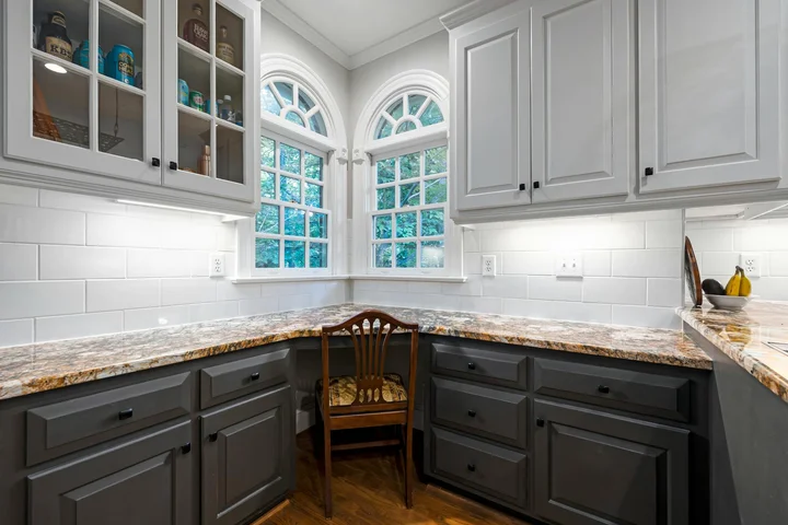 Granite kitchen counter with gray cabinetry, white subway tile backsplash, and an arched window.