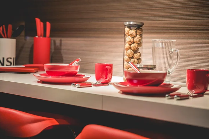 Bright white marble countertop with red plates, cups, and cutlery set for dining; a jar of cookies and a glass pitcher in the background