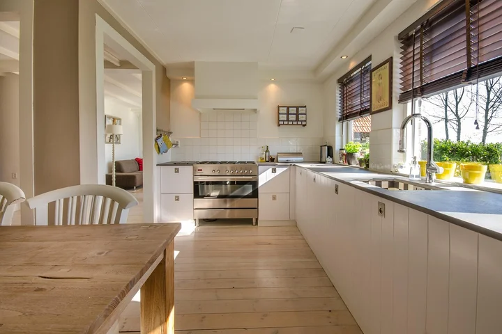 Bright kitchen with white cabinetry, wooden floor, and large windows with blinds; a clean, airy space.