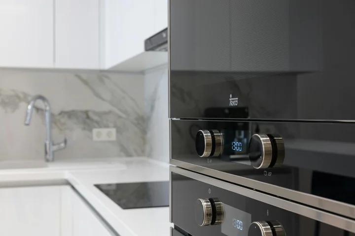 Modern kitchen with a built-in black electric oven and glass-ceramic cooktop, white cabinets, and a marble backsplash.