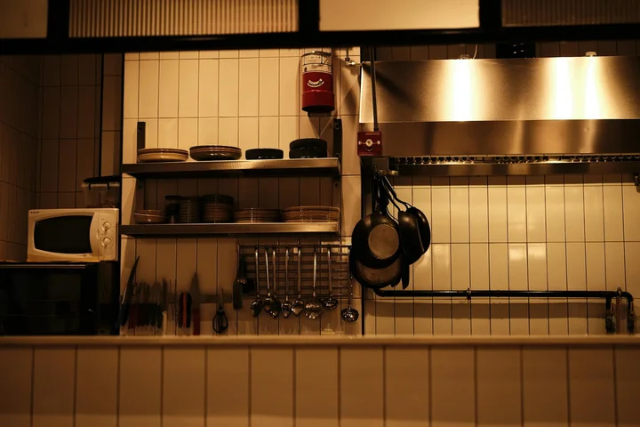 A kitchen featuring a microwave on the counter, open shelves with dishes, and a metal range hood, illustrating a room where burnt odors can linger.