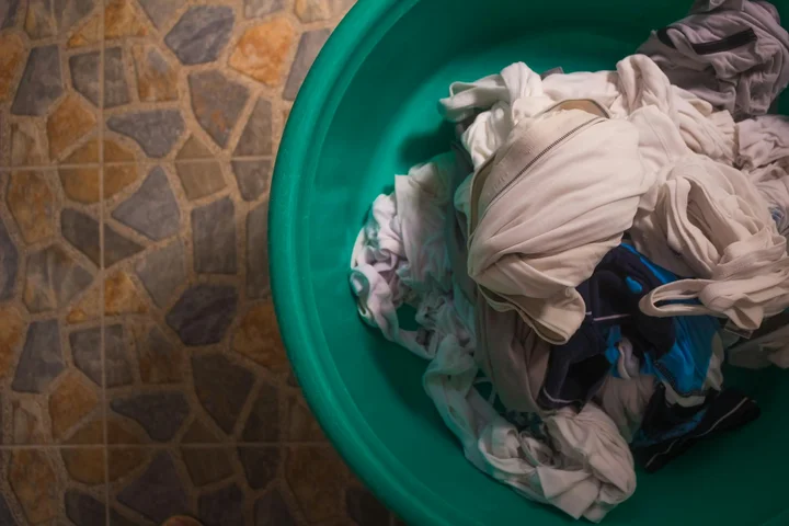 Green plastic laundry bucket filled with wrinkled clothes resting on a tiled floor