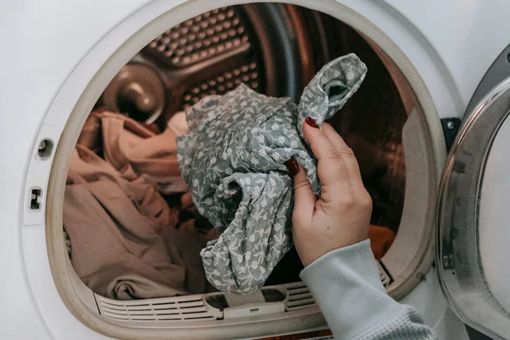 Close-up of a hand holding a gray patterned cloth near an open washing machine drum