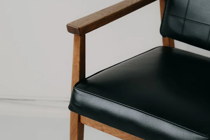 Close-up of a black leather chair with wooden armrests