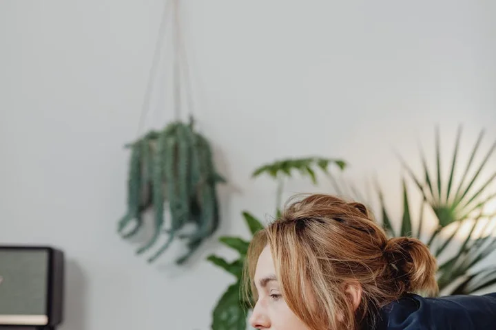 Close-up of a person with light brown hair focusing on a task in a bright room with hanging plants, illustrating careful handling during ink removal.