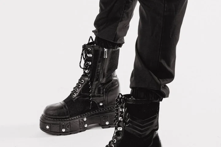Pair of black leather combat boots with laces and zippers, worn with black pants, shown against a light background.