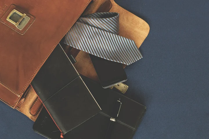 An assortment of leather items on a blue surface: a brown leather bag, wallets, a striped tie, and a few small leather accessories.