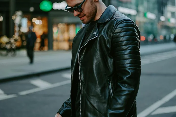 A man in a black leather jacket and sunglasses stands on a city street, illustrating the leather care topic.