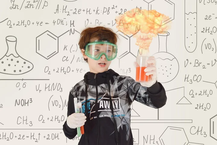 Young student wearing safety goggles, holding a beaker with a flame in a chemistry-themed backdrop illustrating experiments and cleanliness to represent preventing hard water stains.