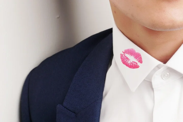 Close-up of a person in a white dress shirt and navy jacket with a pink lipstick kiss mark on the collar.