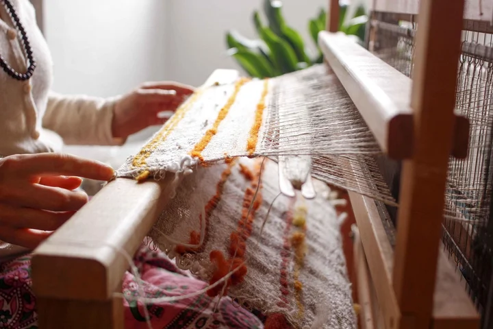 Hands weaving on a loom with colorful fibers forming fabric