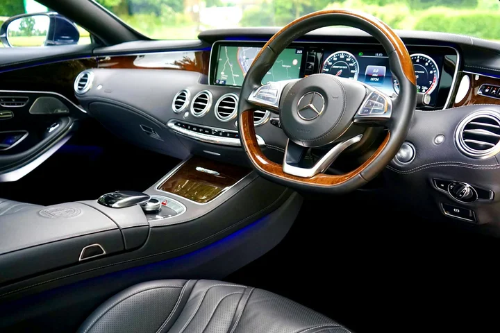 Close-up view of a luxury car interior with leather seats, wood trim, and a steering wheel.