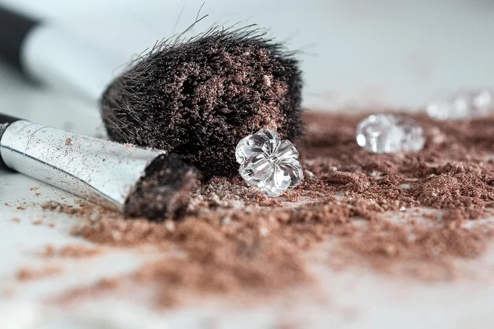 Close-up of a makeup brush with brown powder spilled on fabric and several crystal-like beads nearby
