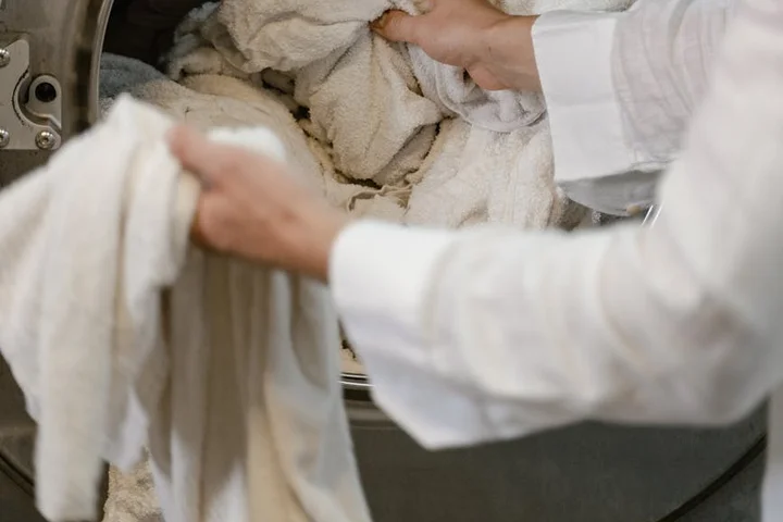 Person loading a washing machine with white towels and clothing.