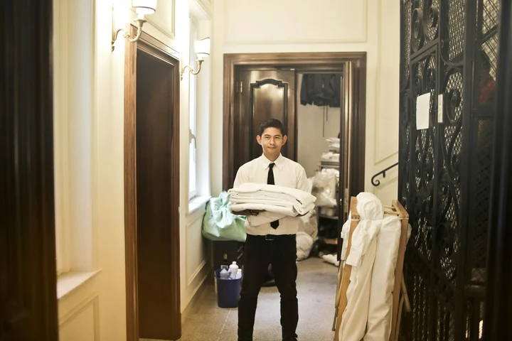 Person in a hallway wearing a white shirt and black tie, holding folded white towels.