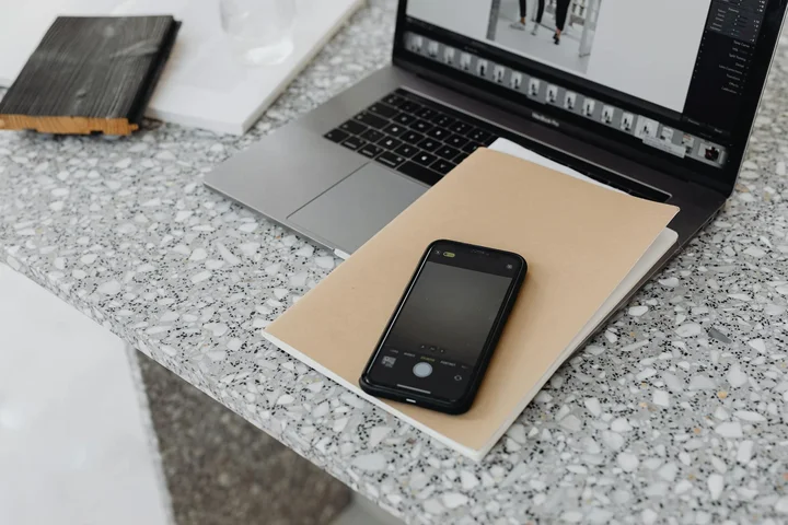 A laptop, notebook, and smartphone sit on a speckled marble countertop, highlighting a tidy workspace for marble stain removal.