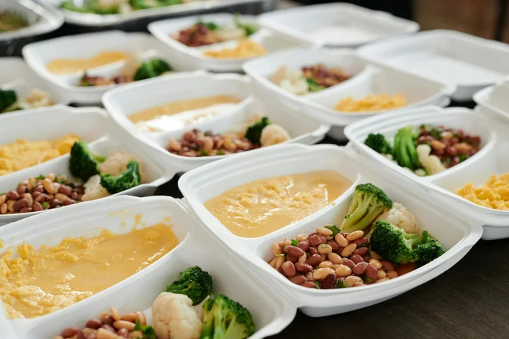 Several white plastic meal prep containers filled with sauce stains and vegetables like broccoli, arranged on a table.