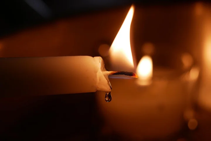 Close-up of a lit candle with melted wax and a dark background, showing wax drips and a burnt wick