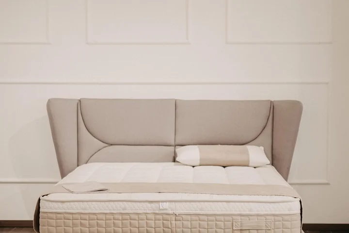 A memory foam mattress with a cushioned headboard in a neutral-colored bedroom.